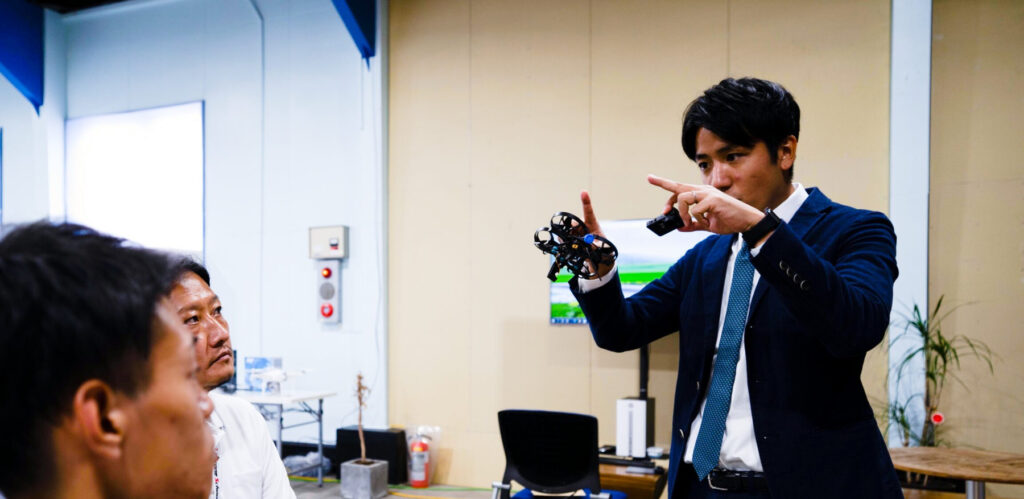 ドローンの機体を手にコンサルティングの説明を行う様子