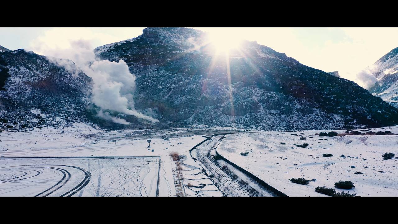太陽の光が差す雪の山と、立ちのぼる噴気。上空から撮影した映像の一場面
